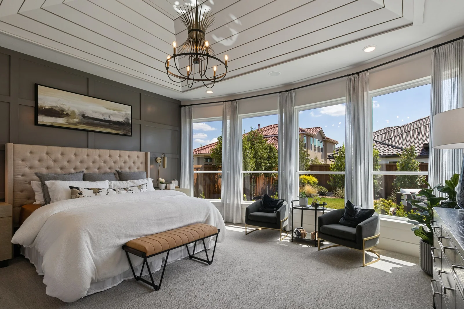 A bedroom with tall windows looking out at the neighboring houses