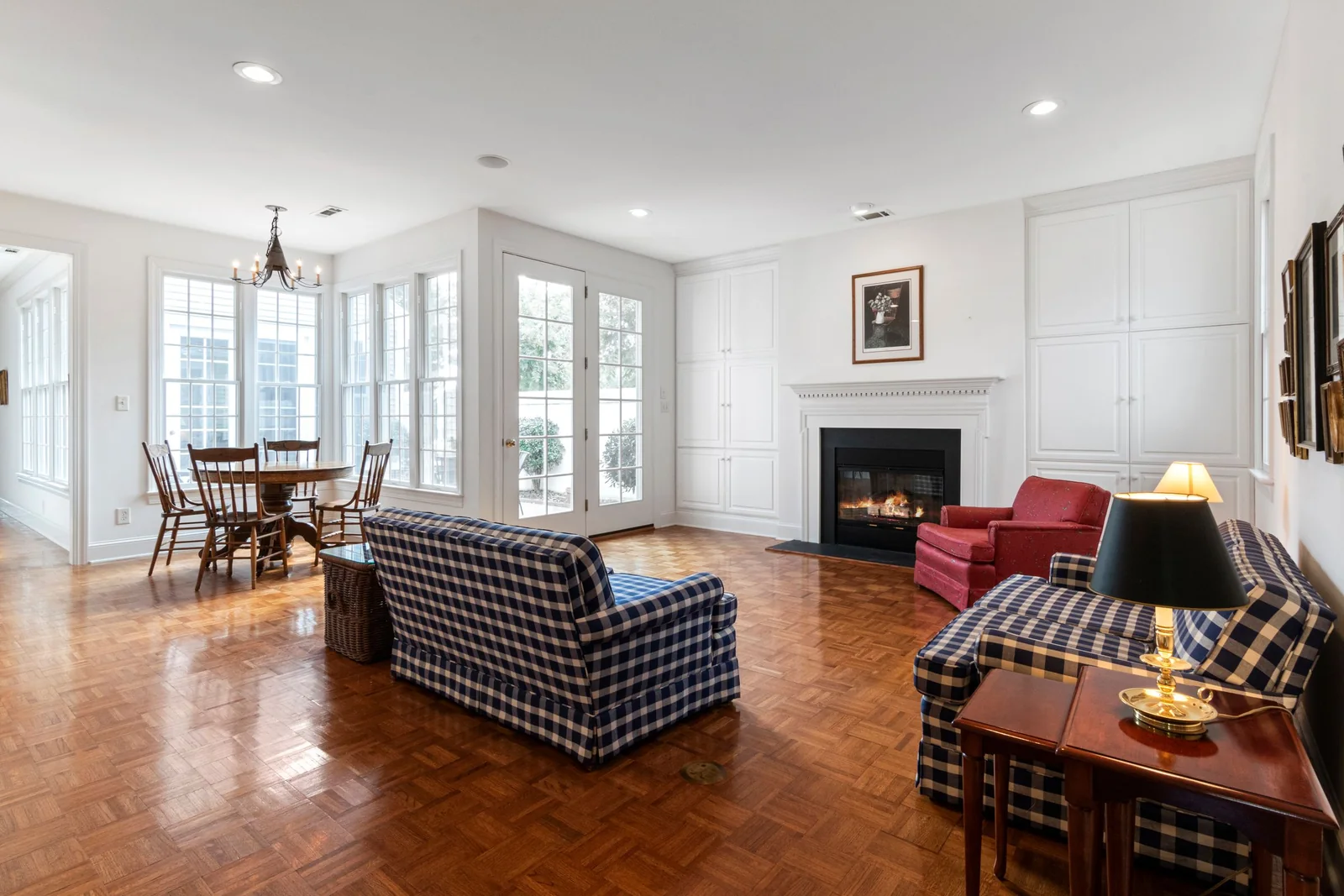 A sunlit living room with hardwood floors and furniture beside tall windows